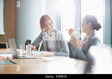 Smiling young businesswomen having lunch at table in office Banque D'Images