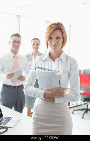 Portrait of businesswoman holding book avec des collègues de bureau à l'arrière-plan Banque D'Images