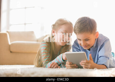 Brother and sister using digital tablet sur le plancher à la maison Banque D'Images