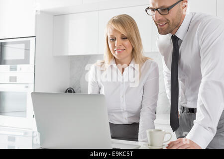 Happy Mid adult woman using laptop au comptoir de la cuisine Banque D'Images