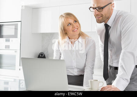 Happy business woman working on laptop in kitchen Banque D'Images