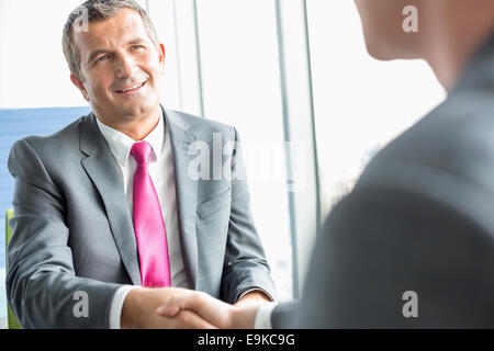 Smiling mature businessman shaking hands with partner in office Banque D'Images