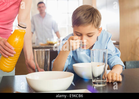 Portrait femme avec jus bouteille debout par fils de prendre le petit déjeuner avec l'homme en arrière-plan Banque D'Images