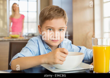 Portrait of boy le petit-déjeuner à table avec mère debout en arrière-plan Banque D'Images