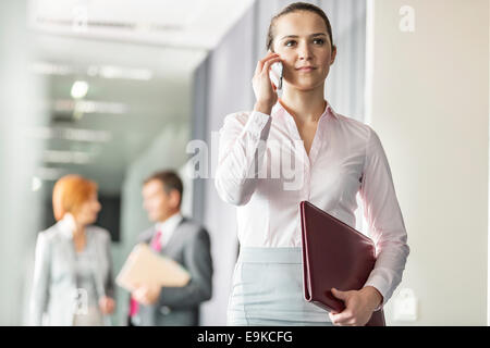 Belle jeune businesswoman on call avec des collègues en arrière-plan à l'office corridor Banque D'Images