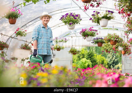 Portrait of happy man watering can in greenhouse Banque D'Images