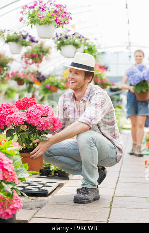 Heureux homme jardinier holding flower pot avec collègue debout en arrière-plan lors des émissions de Banque D'Images