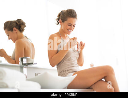 Happy young woman applying nail polish dans salle de bains Banque D'Images