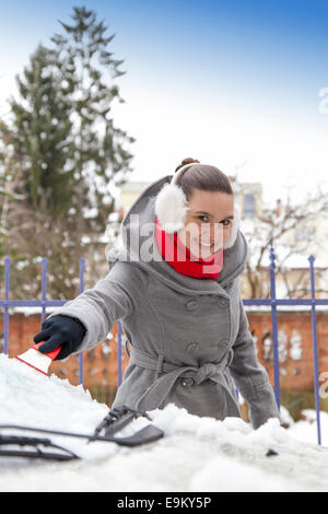 Smiling cute woman enlever la neige de la voiture Banque D'Images