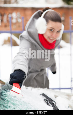 Smiling cute woman enlever la neige de la voiture Banque D'Images