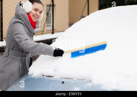 Smiling cute woman enlever la neige de la voiture Banque D'Images