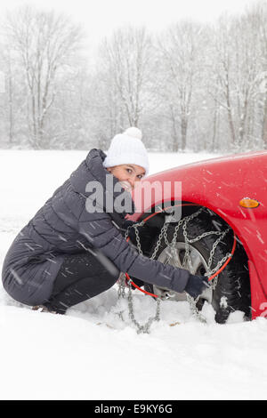 Jeune femme de montage de chaînes de pneu de voiture pilote Banque D'Images