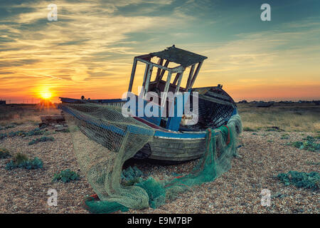 Un vieux bateau de pêche en bois abandonnés avec des filets échoués sur une plage de galets, effet vintage Banque D'Images