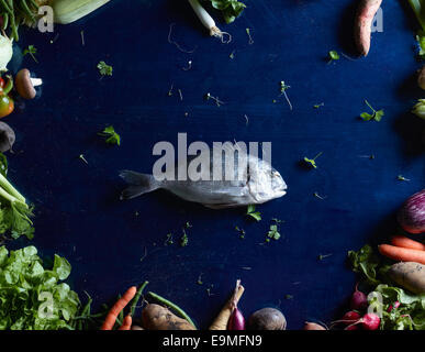 Tourné directement au-dessus de poissons au milieu des légumes sur la table bleu Banque D'Images