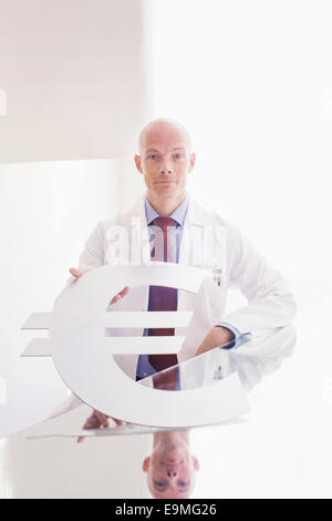 Portrait of male doctor holding symbole de l'euro à 24 en clinique Banque D'Images
