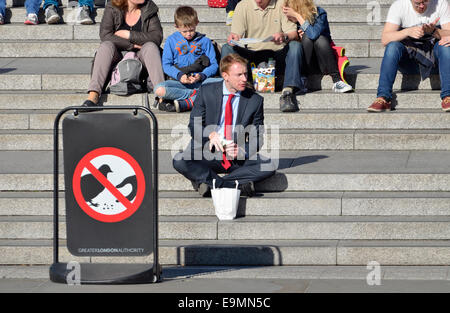 Londres, Angleterre, Royaume-Uni. L'homme de manger sur les marches de la National Gallery à Trafalgar Square. 'Ne pas nourrir les pigeons' sign Banque D'Images