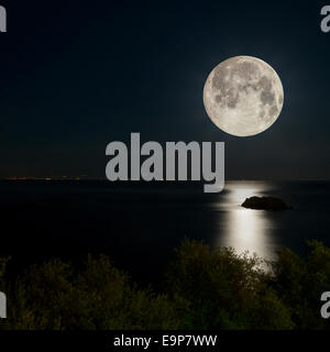 Scène de nuit. Pleine lune reflétée sur la mer. Les lumières de la ville, à l'horizon. Banque D'Images