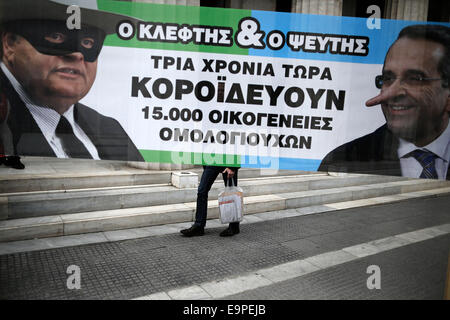 Thessalonique, Grèce. 31 octobre, 2014. Un homme marche derrière une bannière avec des caricatures de Grèce est vice-Premier Ministre et Ministre des affaires étrangères Evangelos Venizelos à gauche et le Premier Ministre grec Antonis Samaras qui lit 'Le menteur et le voleur" au cours d'une manifestation devant la direction générale de la Banque de Grèce. À l'occasion de l'épargne mondiale Journée environ 50 petits obligataires qui ont subi des pertes importantes au cours de l'énorme dette publique radiation sur 2012, affirment avoir été trompés par le gouvernement et demandent une indemnisation. Thessalonique, Grèce le 31 octobre 2014. Credit : Konstantinos Tsakalidis/Alamy Live News Banque D'Images