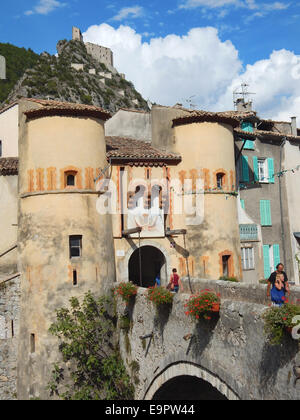 Festung und Stadttor à Entrevaux - Touristen schlendern ueber die alte Bruecke zum historischen Ortskern des wehrhaften Dorfes, dass der historischen Schmalspurbahn zwischen Nizza und Digne-les-Bains in den Bergen liegt. Zur Roemerzeit lag hier eine keltisch-ligurische Siedlung am Fluss Var - 1690 beauftragte Koenig Ludwig XIV. den franzoesischen Militaerarchitekten Vauban, den Ort mit Befestigungsanlagen besser zu schuetzen. Banque D'Images