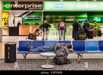 Tôt le matin à l'aéroport Gatwick de Londres, Royaume-Uni. Un coin couchage backpacker étiré le long d'une rangée de sièges à l'avant de la voiture de location d'un bureau Banque D'Images