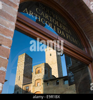 San Gimignano, Toscane, Italie. Tours médiévales reflète dans la fenêtre d'un magasin de souvenirs sur la Piazza della Cisterna. Banque D'Images