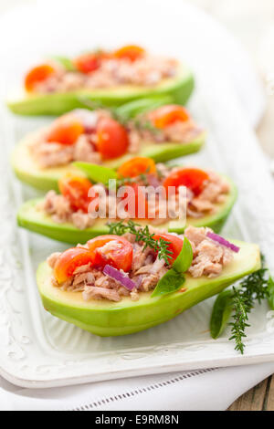 Avocat farci au thon, oignons rouges, tomates cerises et herbes. Banque D'Images