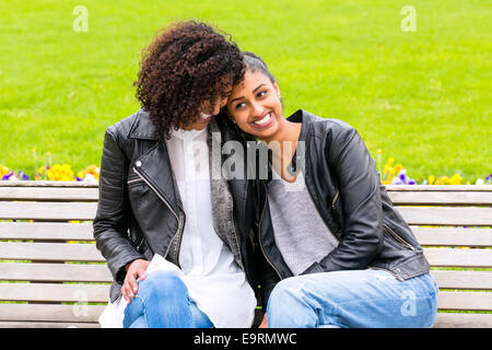 Deux adolescents d'Afrique du Nord friends sitting together on park bench talking Banque D'Images