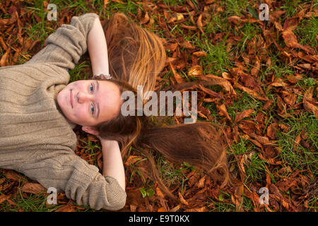 Jeune jolie fille gisant sur le sol avec des feuilles mortes en automne parc. Banque D'Images