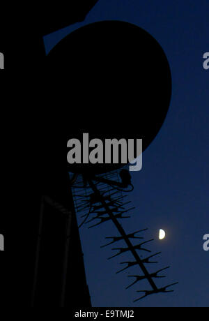 Antenne et parabole satellite silhouetté contre un ciel de pleine lune. Banque D'Images