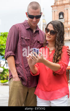 Jeune couple smartphone contrôle tout en marchant dans la ville de Puerto Vallarta, Mexique. Banque D'Images