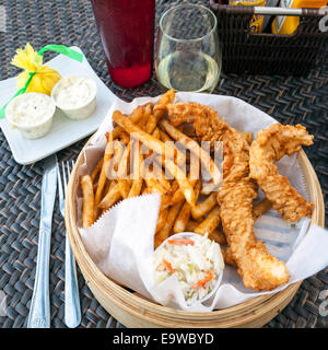 Fish and chips corbeille avec flet battues, croustillant, assaisonnée de frites, de salade de chou, sauce tartare et un verre de vin blanc. Banque D'Images