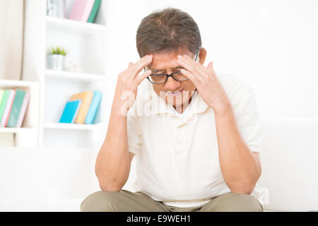 Portrait of mature Asian man ayant des maux de tête, assis sur le canapé à la maison, retraité vivant à l'intérieur de vie. Banque D'Images