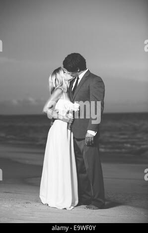 Beau couple de mariage, mariée et le Marié baiser sur la plage au coucher du soleil. Photographie noir et blanc Banque D'Images