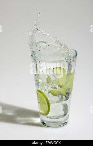 Des cubes de glace tomber dans un verre d'eau et de la chaux Banque D'Images