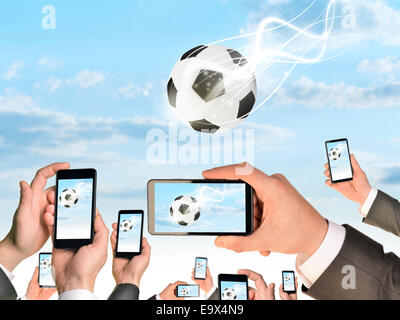 Mains tenant des téléphones intelligents et des vidéos comme relevant d'un ballon de football Banque D'Images