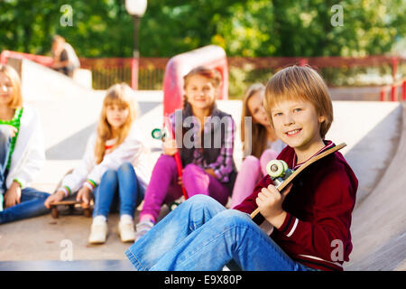 Garçon avec skateboard et ses amis assis derrière Banque D'Images