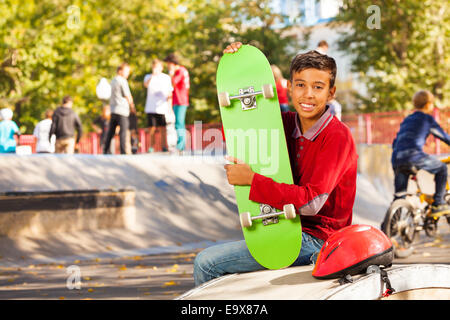 Heureux garçon arabe avec green skateboard assis Banque D'Images