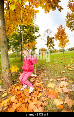 Girl est assis sur des balançoires en maintenant le parc à cordes Banque D'Images