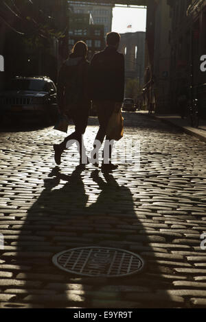 Silhouettes de deux jeunes personnes se tenant la main descendre rue pavée de Brooklyn coucher du soleil Banque D'Images