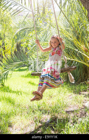 Girl sitting on tree swing swinging in garden Banque D'Images