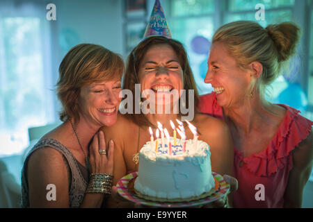 Young woman holding birthday cake, ce désir alors que deux amis rechercher sur Banque D'Images