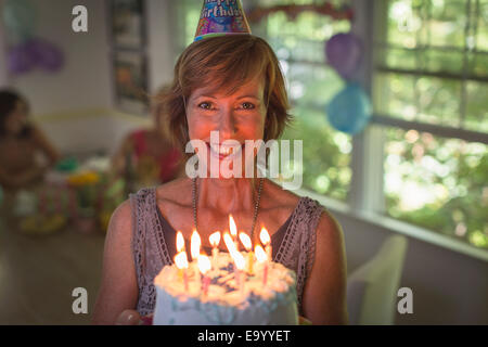 Portrait of mature woman holding birthday cake with candles Banque D'Images