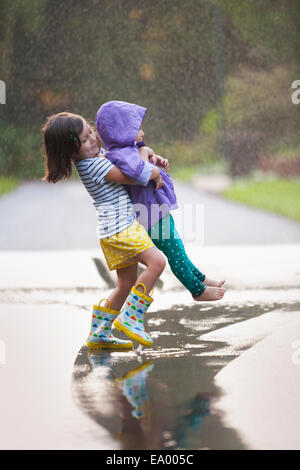 Transport tout-petit fille soeur par flaque sur street Banque D'Images