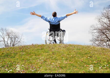 Heureux utilisateur de fauteuil roulant sur une colline verte Banque D'Images