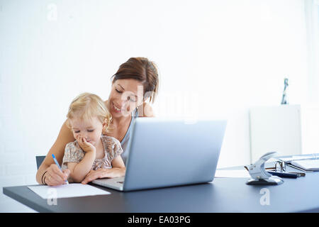 Mid adult woman writing notes avec toddler fille sur ses genoux Banque D'Images