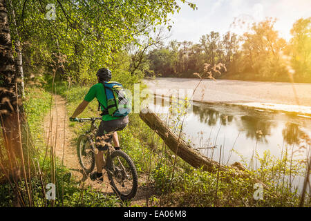 Vue arrière du jeune homme à vélo sur le chemin Riverside Banque D'Images