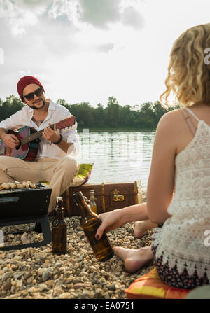 Jeune homme assis au bord du lac à jouer de la guitare Banque D'Images