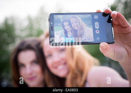 Portrait de deux jeunes amies en tenant sur smartphone selfies dans park Banque D'Images