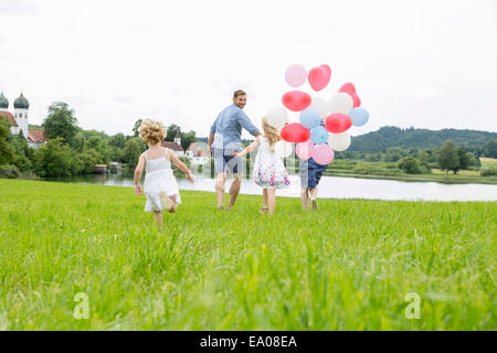 Family running through field with balloons Banque D'Images