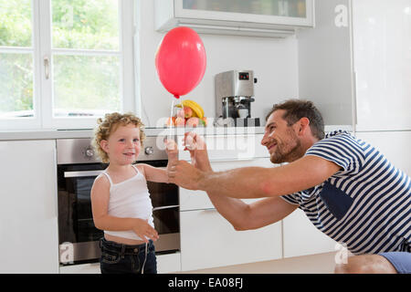 Girl holding balloon avec le père dans la cuisine Banque D'Images